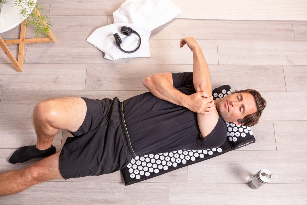 Man lying on the LyfeFocus Acupressure Mat and Pillow, using it during a floor stretch at home